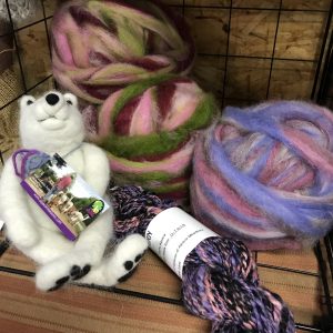 Purple and green wool sits beside a wool felted polar bear