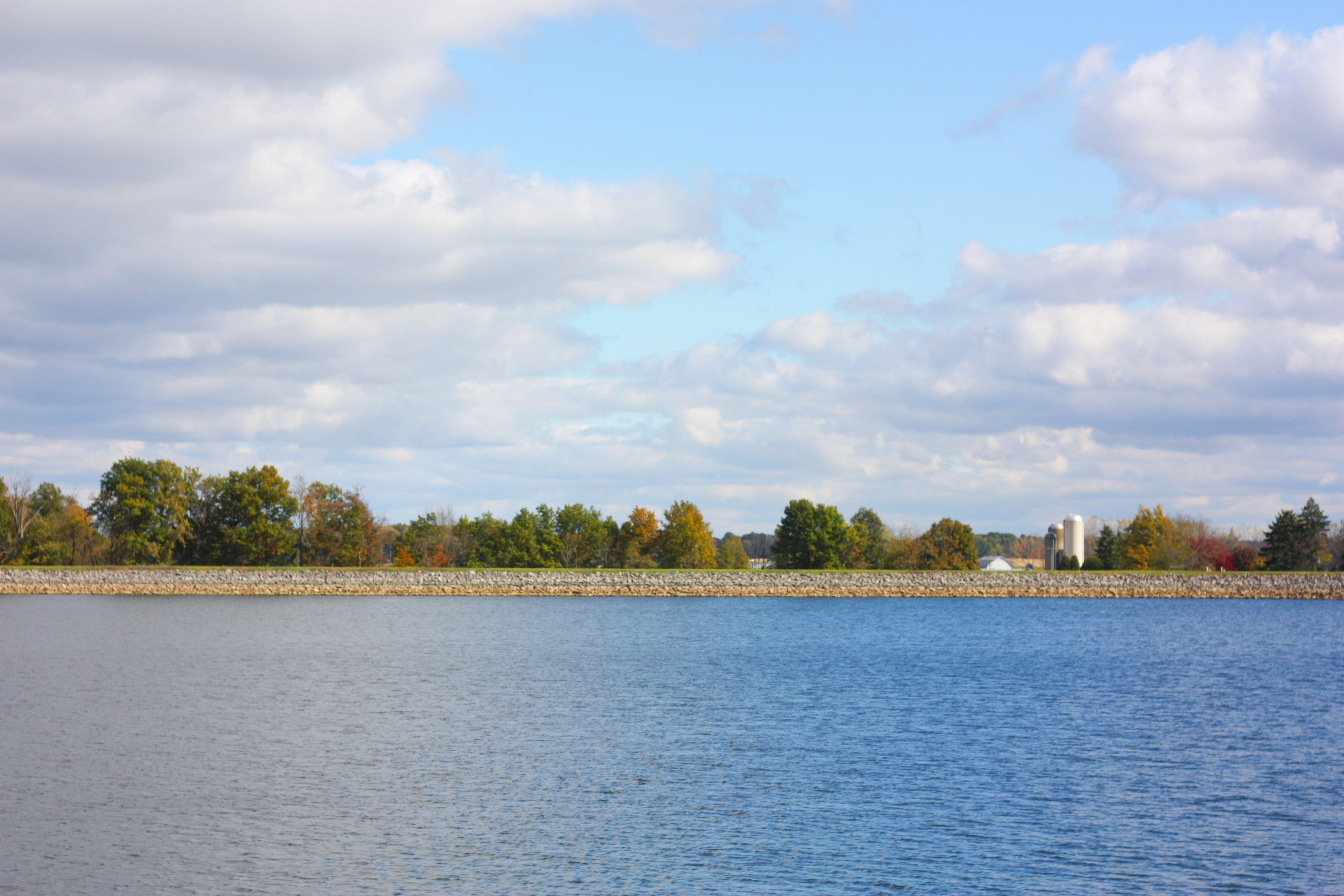 Blue lake with fall trees and a farm in the distance